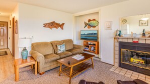 Un salon comprenant un canapé, une table basse, un téléviseur, une cheminée et un décor mural représentant des poissons.