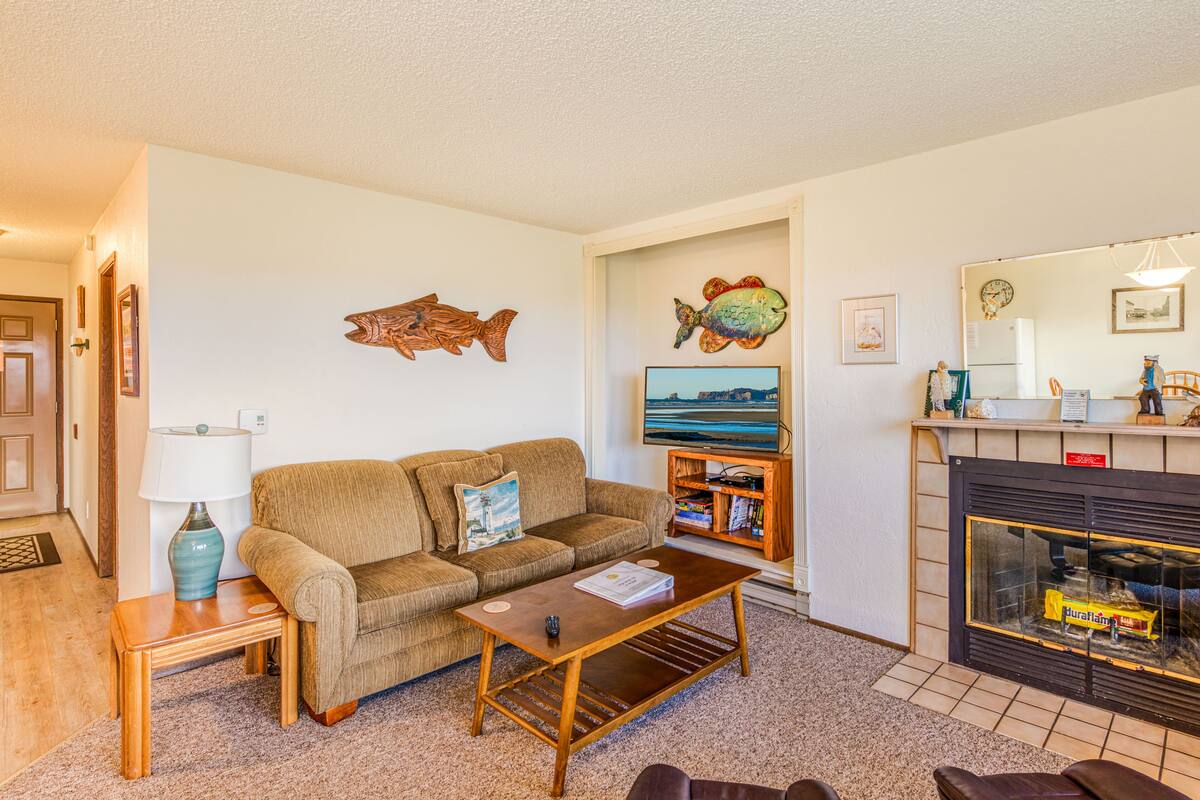 A living room with a sofa, coffee table, TV, fireplace, and decorative fish wall art.