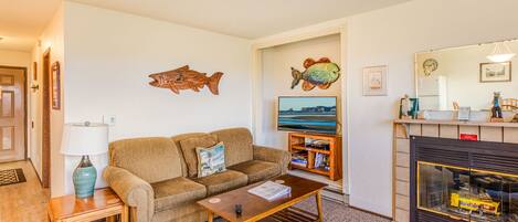 Una sala de estar con sofá, mesa de centro, televisión, chimenea y un cuadro de peces decorativos.