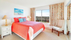 Une chambre avec un grand lit, une chaise, une table de chevet, une fenêtre donnant sur un beau paysage et des rideaux.