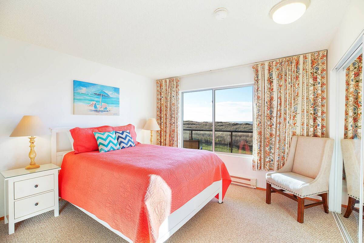 A bedroom with a large bed, a chair, a nightstand, a window with a view, and curtains.