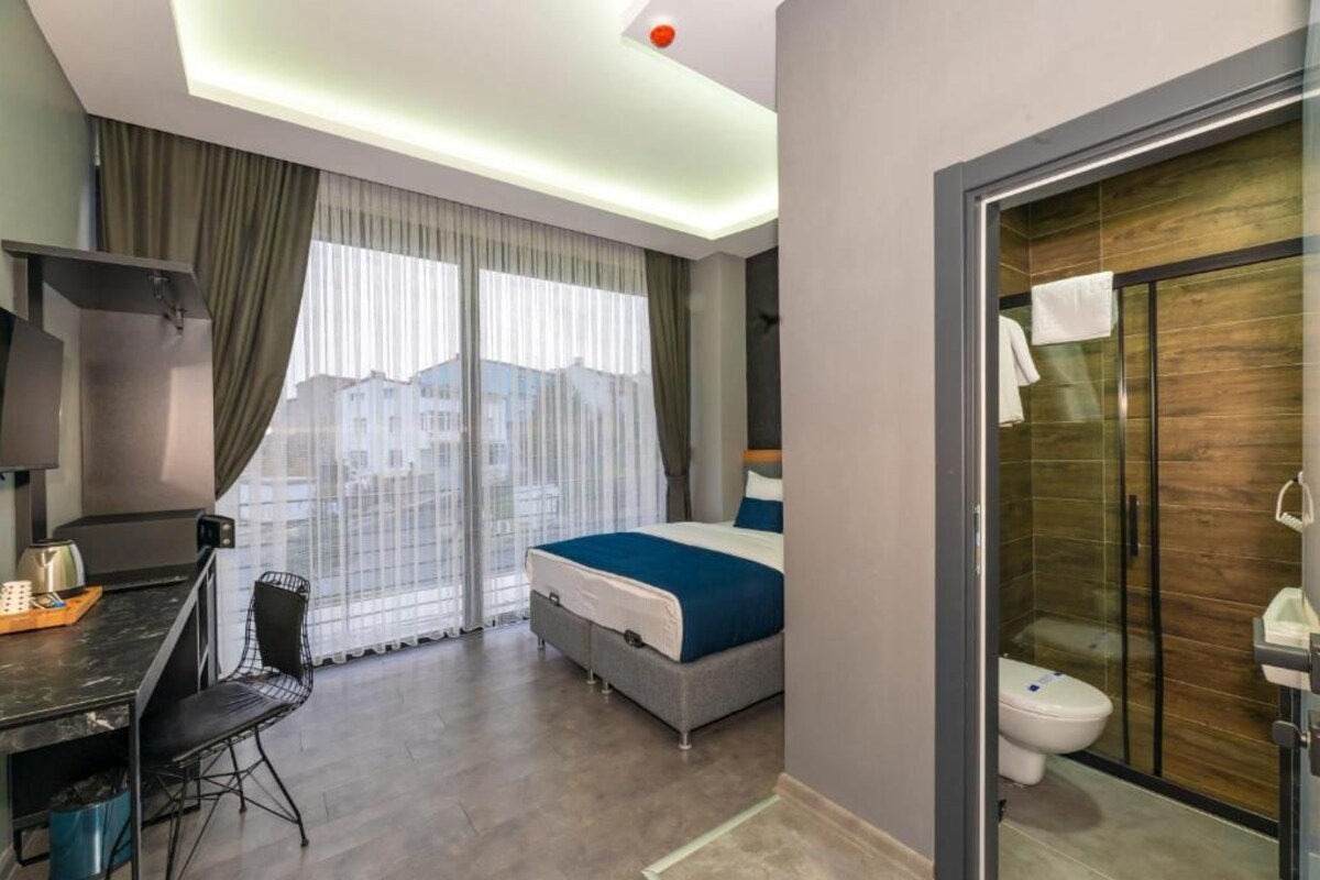 Une chambre d’hôtel moderne équipée d’un lit, d’un bureau, d’une chaise, d’une douche et offrant une vue sur la ville par la fenêtre.