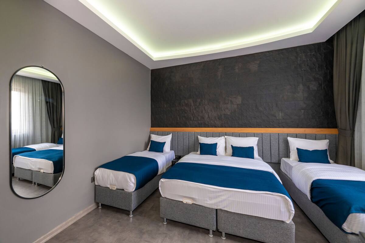 A hotel room with four beds arranged in a row, a large mirror, and a modern ceiling design.