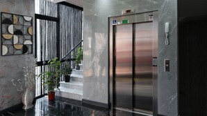 Een moderne lift met een digitaal display, een rolstoeltoegankelijkheidsbordje en een telefoon aan de muur.