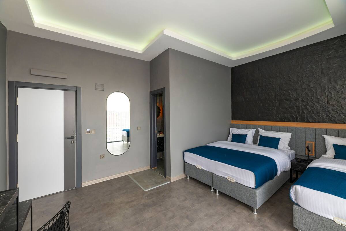 A modern hotel room with two beds, a large mirror, and a stone-textured accent wall.