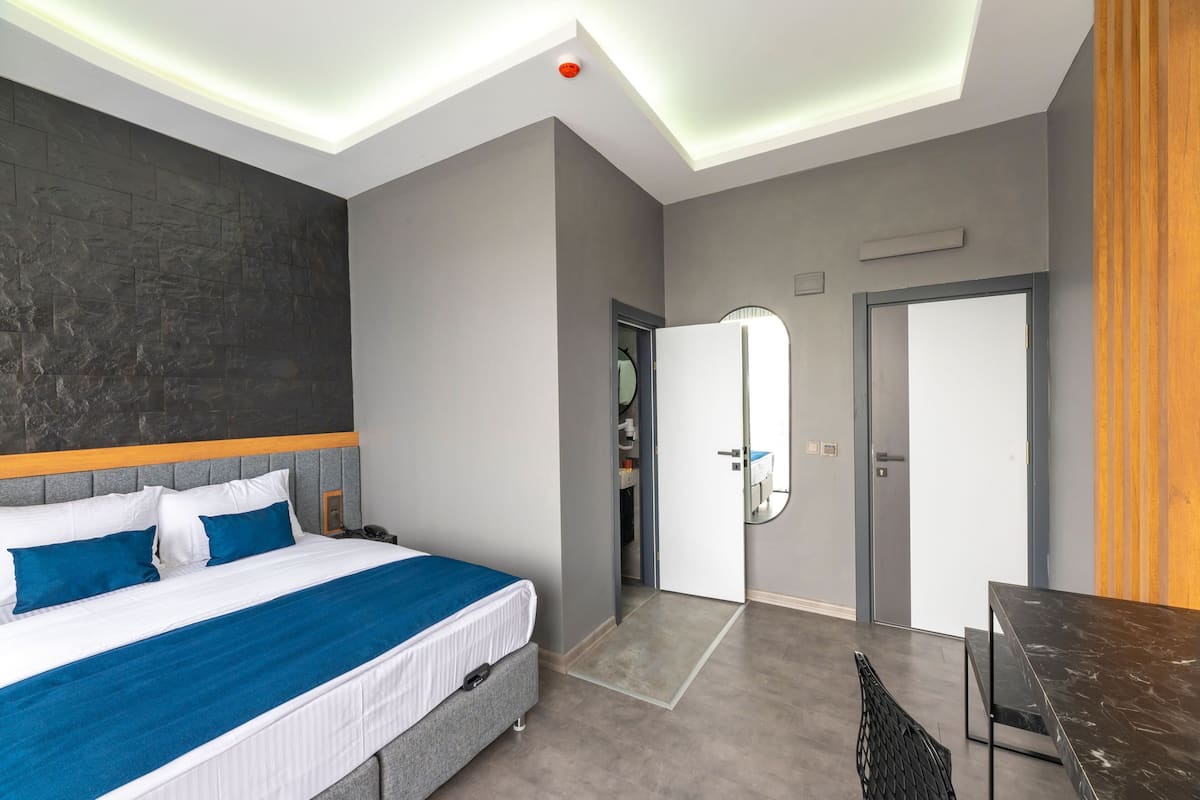 A modern hotel room with a large bed, a desk, and a wardrobe.