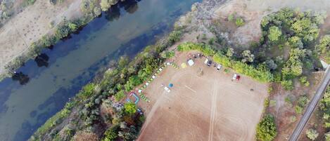 An aerial view of a campsite with tents, a dirt field, and a river.