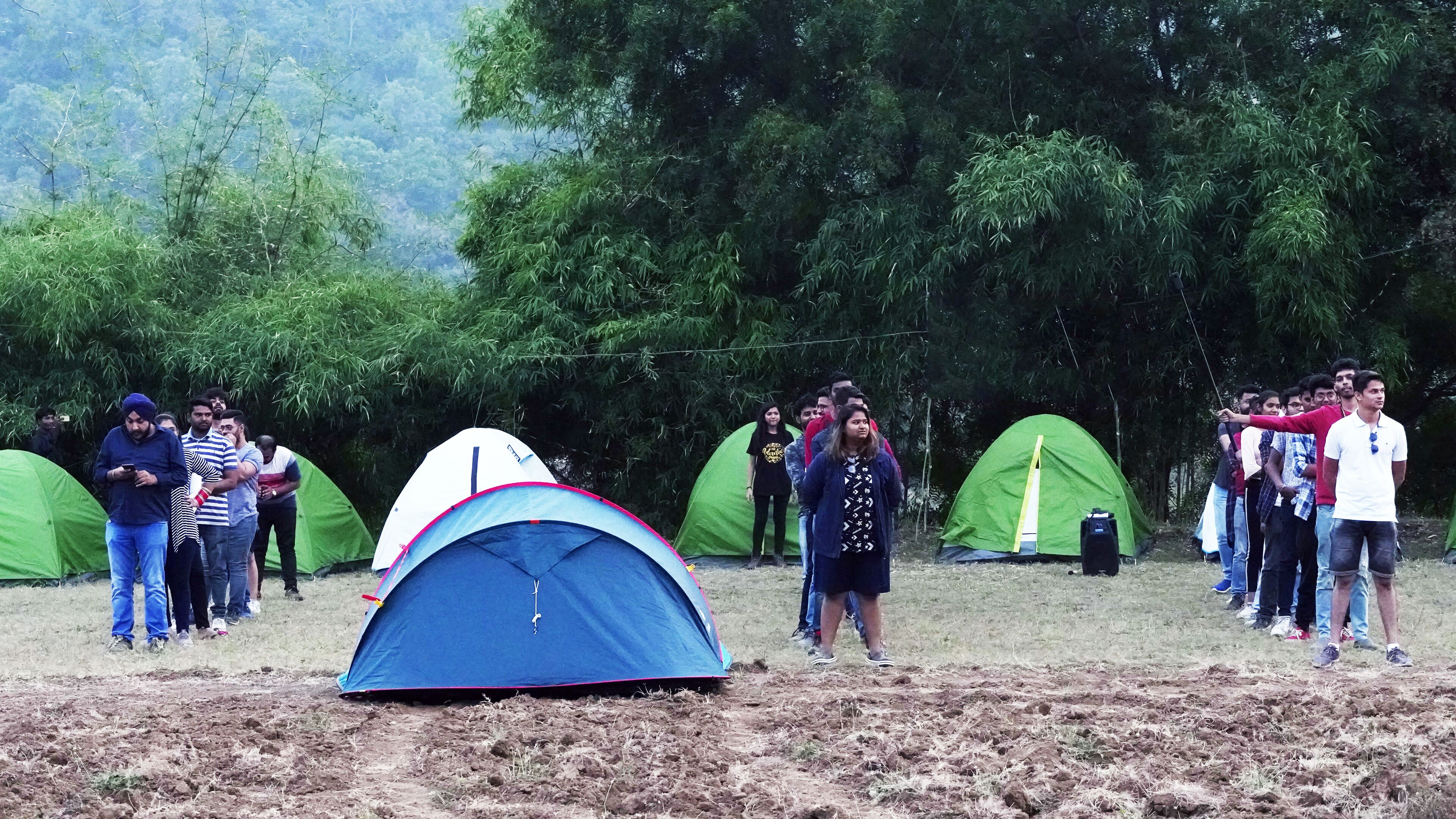 Un groupe de personnes se tient debout autour de tentes dans un champ, avec des arbres en arrière-plan.