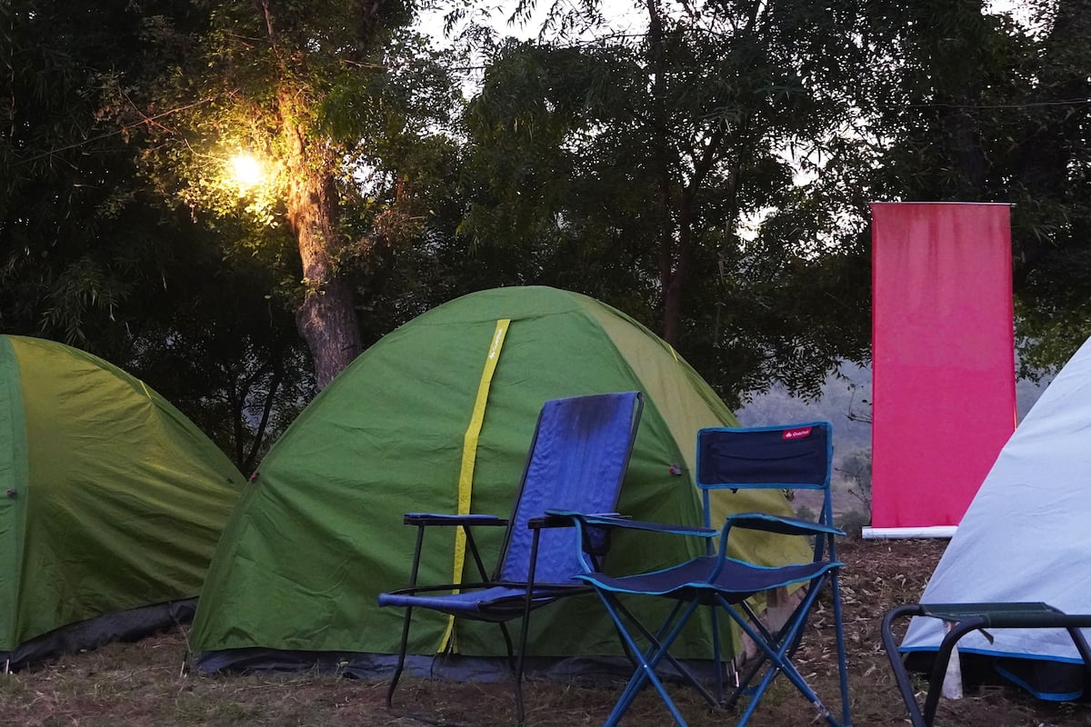 Two green tents, a blue folding chair, and a red structure in a campsite.