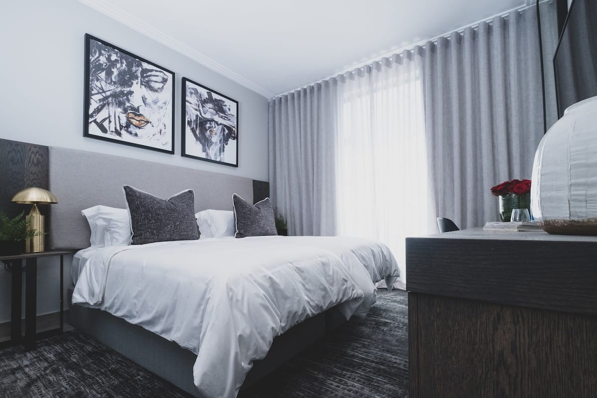 Una habitación de hotel moderna con una cama grande, cortinas grises y dos cuadros enmarcados en la pared.