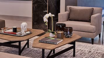 Un soggiorno moderno con un divano beige, due tavolini in legno, una parete in marmo e un tappeto decorato.