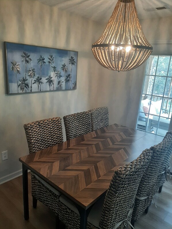 A dining area with a large wooden herringbone table, woven chairs, a hanging light fixture, and a painting of palm trees on the wall. - Easy Walk to Beach, Concerts, Publix, Splash Pad, Market.
Bikes, Carts, & Chairs (Oak Island)