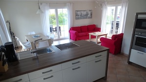 Una cocina moderna con una isla central, armarios blancos y un sofá rojo en la zona de estar.