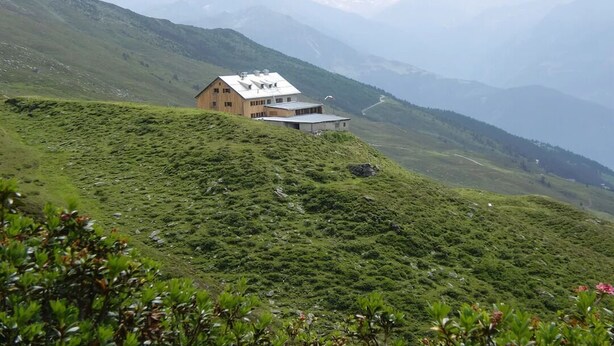 A mountain lodge with a sloped roof, surrounded by lush greenery and distant mountains. - Haus Guenther, vacation apartment for families, couples or singles. (Aschau im Zillertal)