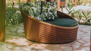 Una estructura con techo de paja, un banco de mimbre y plantas en macetas.