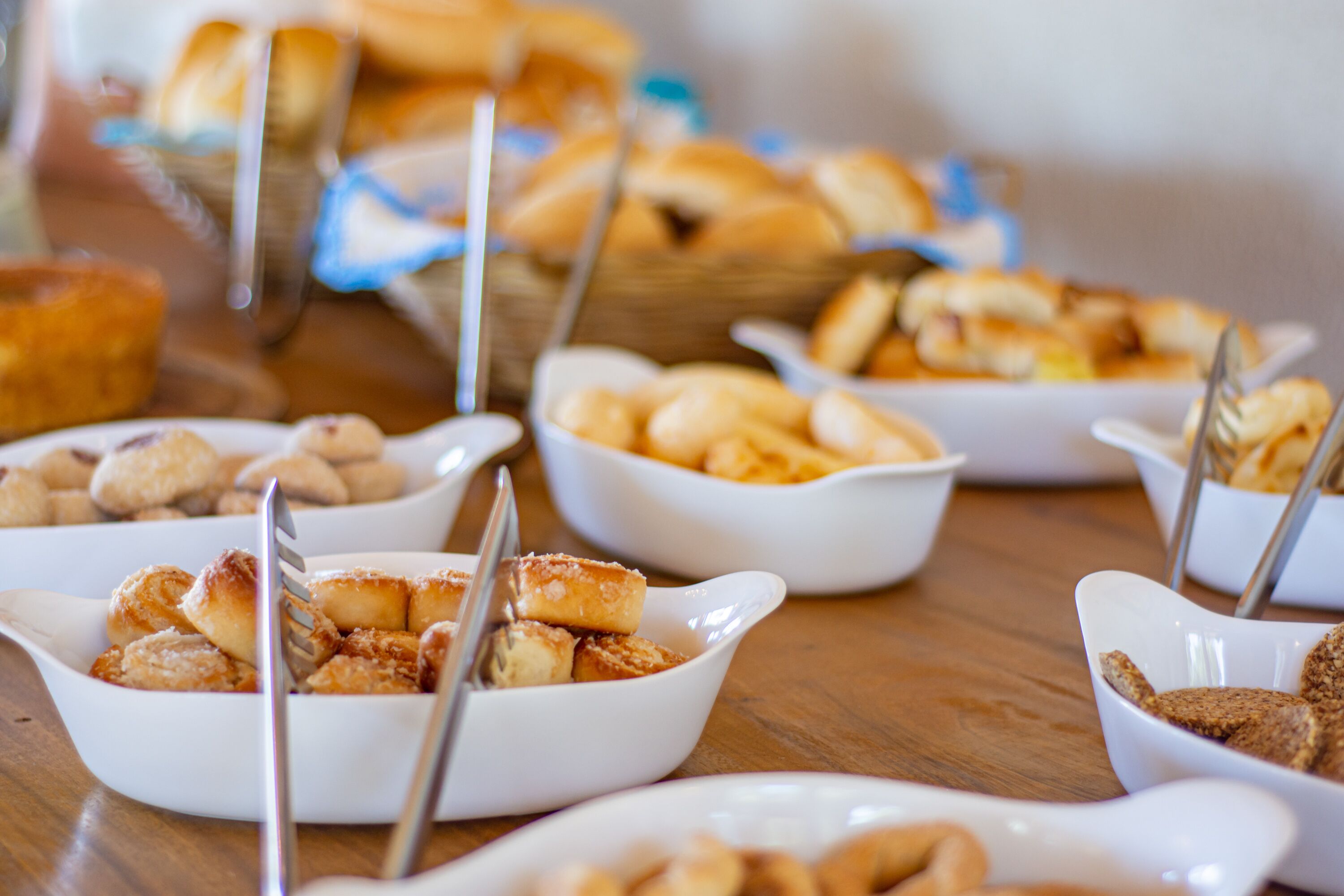 Una mesa de buffet con diversos alimentos en cuencos blancos, incluyendo pasteles y pan.