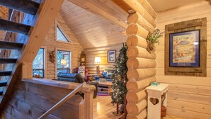 A log cabin interior with a staircase, a Christmas tree, a framed picture, and a cozy seating area. - Third night free on stays before 9/8/26 (Rhododendron)