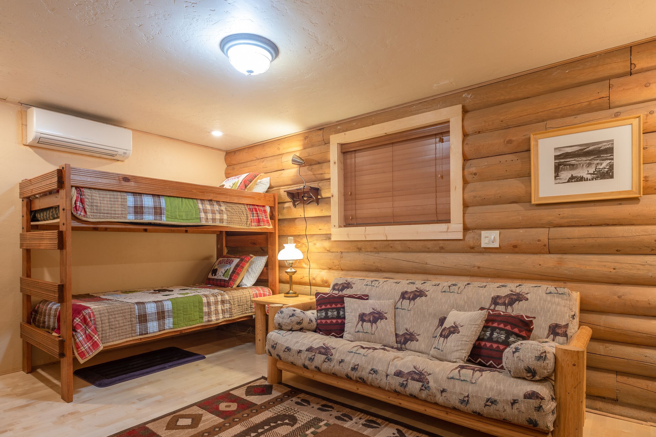 A cozy cabin room with a bunk bed, a sofa with animal prints, a wooden wall, and a framed picture.