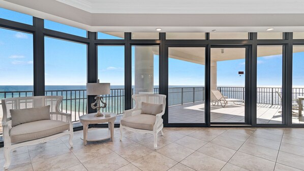 A spacious balcony with a view of the ocean, furnished with two chairs and a small table.