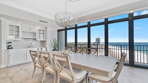 A spacious kitchen with white cabinets, a large island, and a view of the beach through expansive windows.