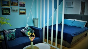 Een moderne slaapkamer met een blauwe bank, een bed met blauw beddengoed, en een klein rond tafeltje met een bloevas.