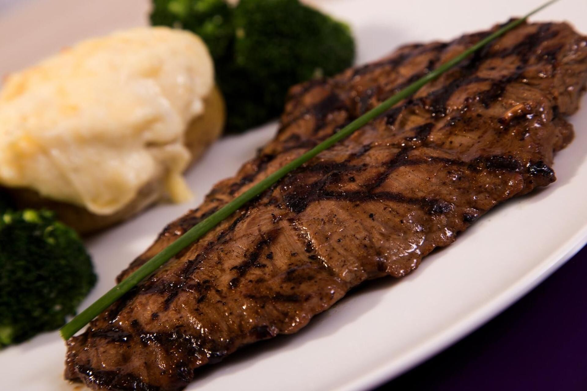 A grilled steak with a garnish of chives, accompanied by a side of mashed potatoes and steamed broccoli.