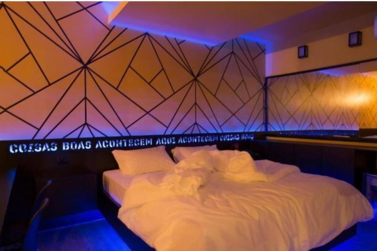 Une chambre d’hôtel avec un mur orné d’un motif géométrique, un lit parfaitement fait et un mini-bar.