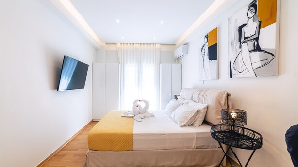 A modern hotel room with a bed, a flat-screen TV, artwork on the walls, and a bedside lamp. - D9 center of Glyfada (Glyfada)