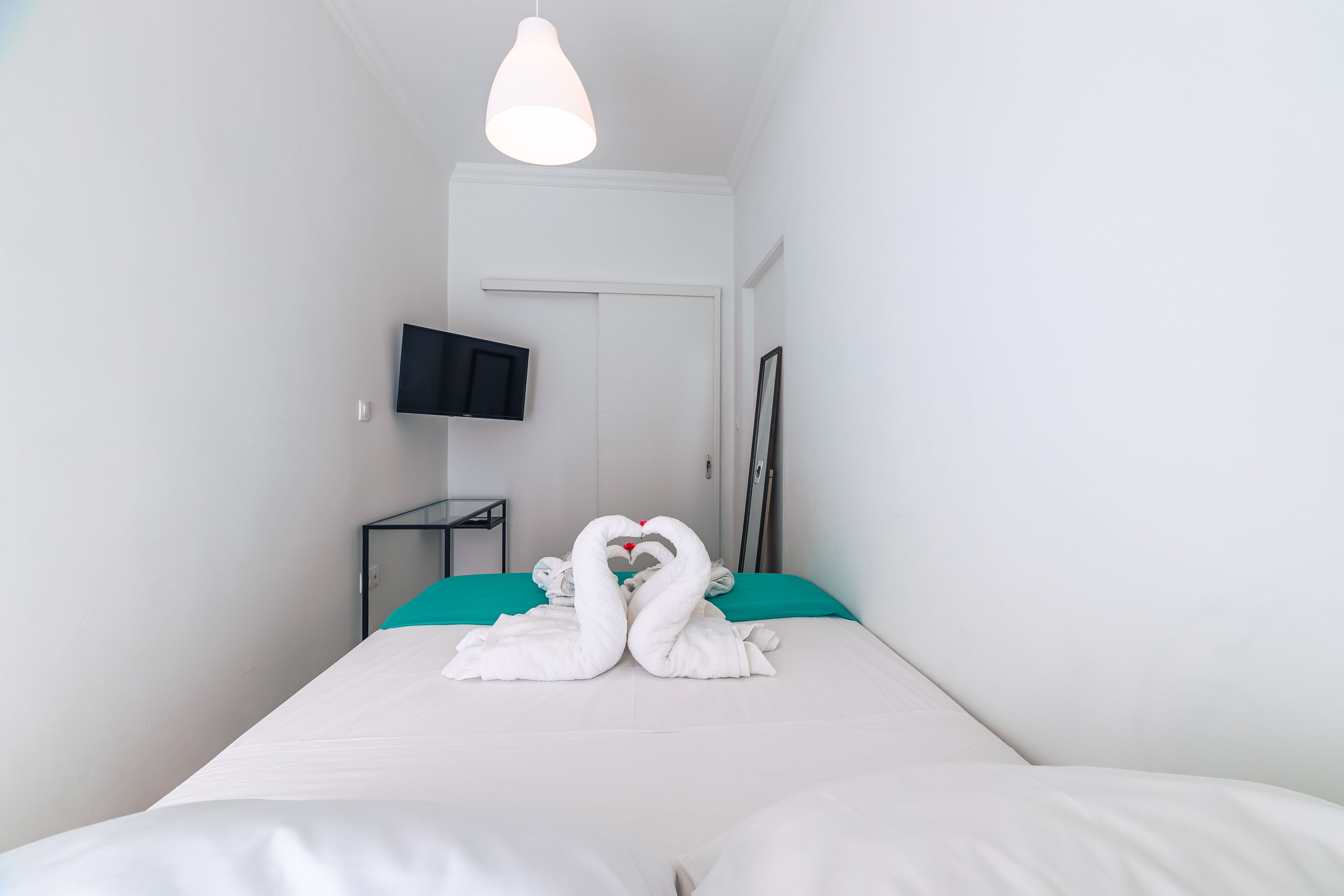 A hotel room with a bed, a flat-screen TV mounted on the wall, and a door.