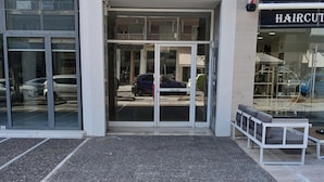 A building entrance with glass doors, a bench outside, and a sign for a hair salon visible through the glass. - D9 center of Glyfada (Glyfada)