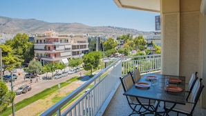 A balcony with a table set for dining, overlooking a street with buildings and a hilly landscape. - D9 center of Glyfada (Glyfada)