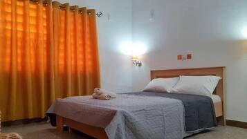 Un dormitorio con una cama, una mesita de noche, una lámpara y una ventana con cortinas.
