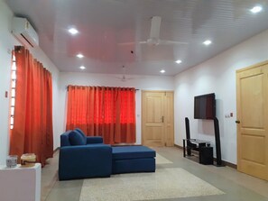 A living room with a blue sofa, red curtains, a ceiling fan, and a TV on a stand.