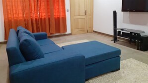 Una habitación con un sofá azul, una puerta de madera y un televisor montado en la pared.