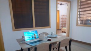 Un comedor con una mesa, sillas, una computadora portátil y una ventana con persianas.