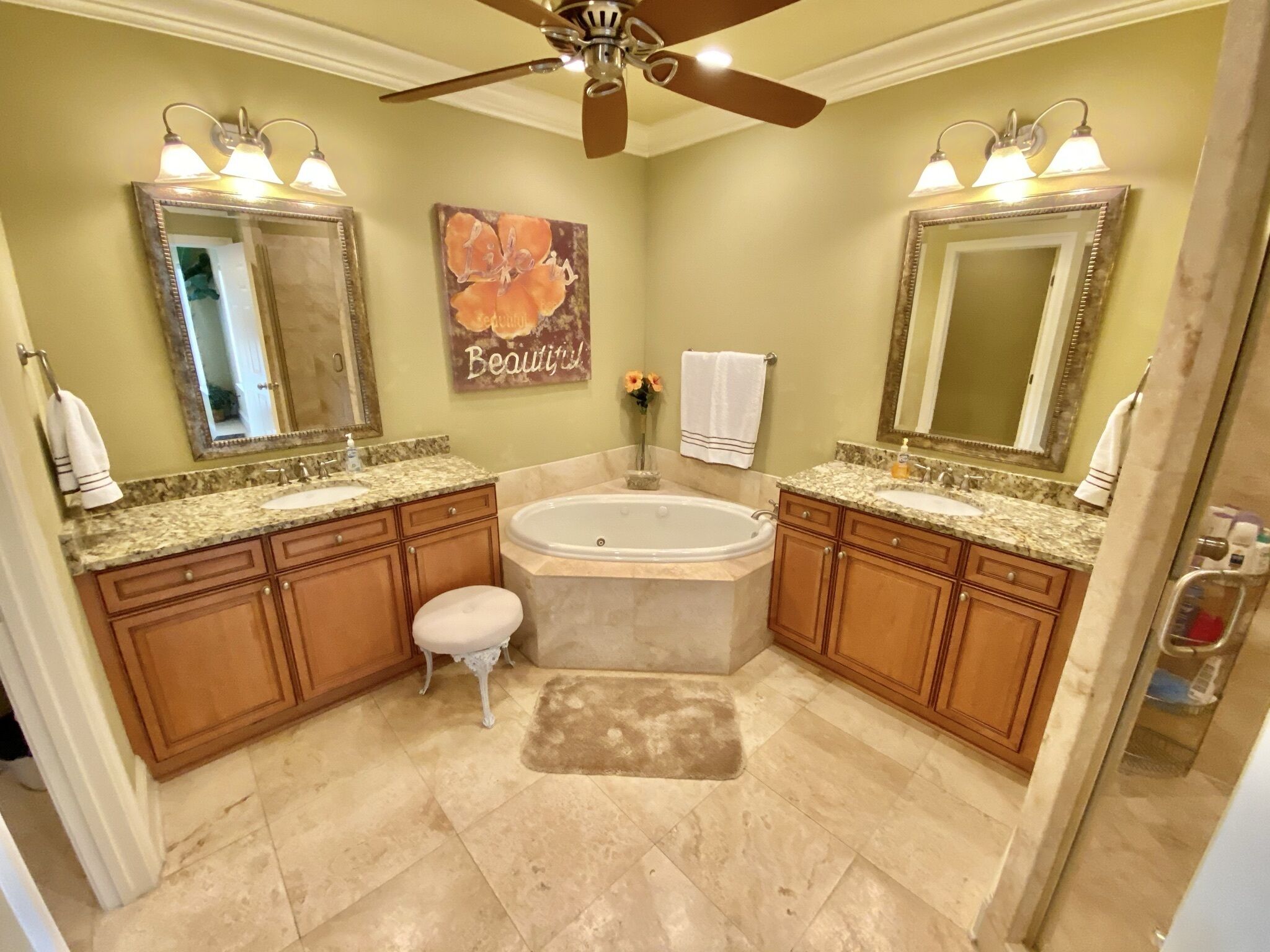 A bathroom with two sinks, a large bathtub, wooden cabinets, a ceiling fan, and a mirror with lights.