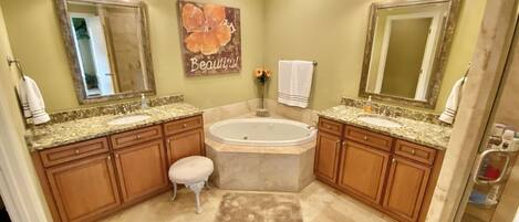 A bathroom with two sinks, a large bathtub, wooden cabinets, a ceiling fan, and a mirror with lights.