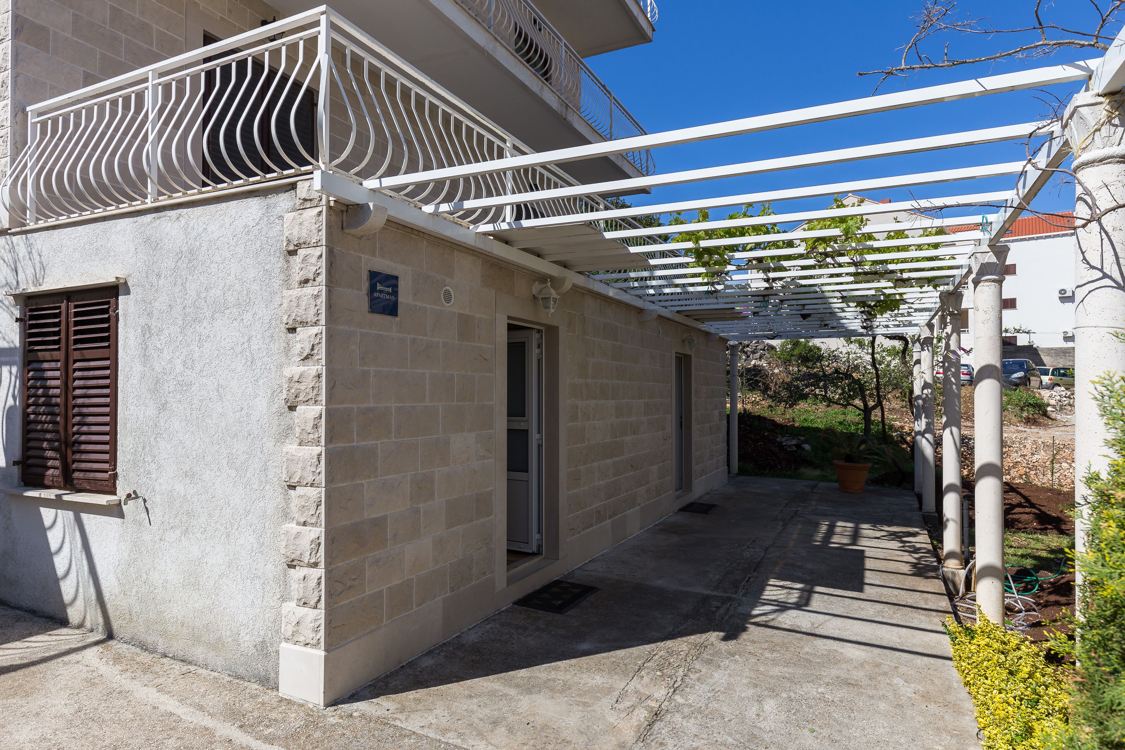 A building with a stone facade, a balcony with a white railing, and a covered outdoor area with a pergola.