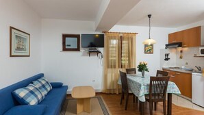 Ein kompakter Wohnbereich mit einer Couch, einem Esstisch mit Stühlen, einem Fernseher und einer Küchenzeile.
