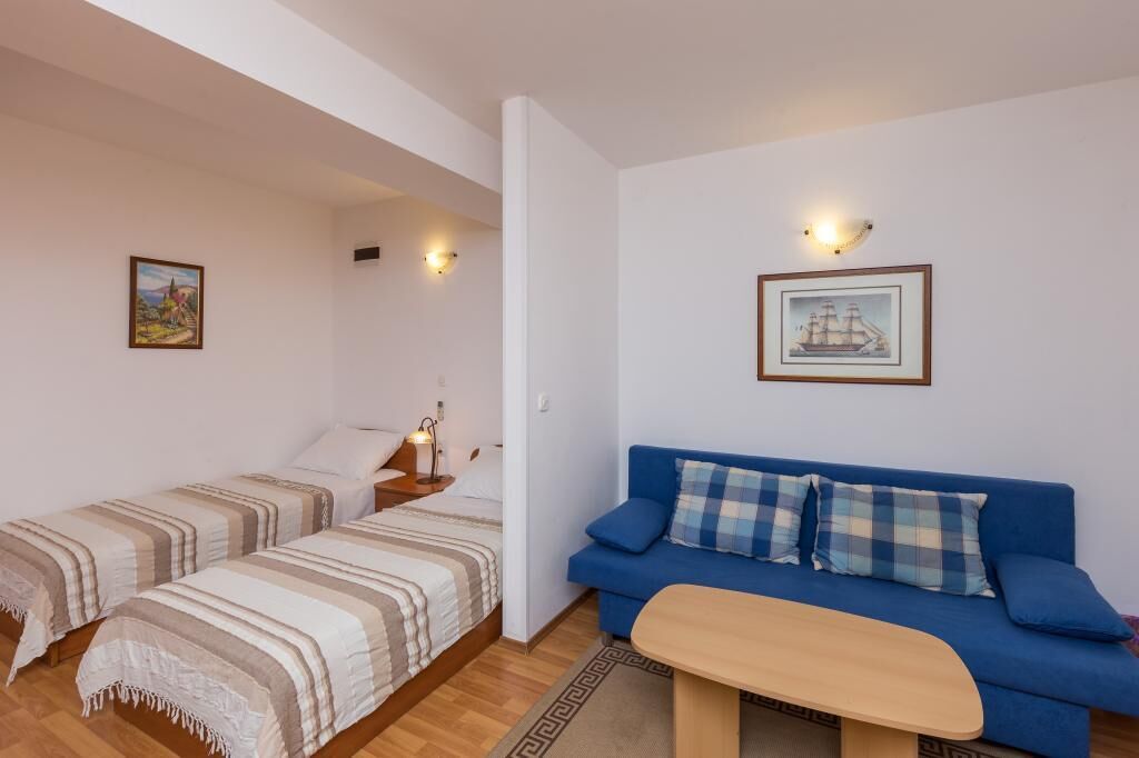 A room with two single beds, a blue sofa, a small table, and wall-mounted lights.