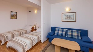 Ein Zimmer mit zwei Einzelbetten, einem blauen Sofa, einem kleinen Tisch und Wandleuchten.