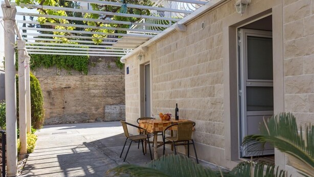 Eine überdachte Terrasse mit Tisch und Stühlen, einer Pergola und einer Steinmauer.