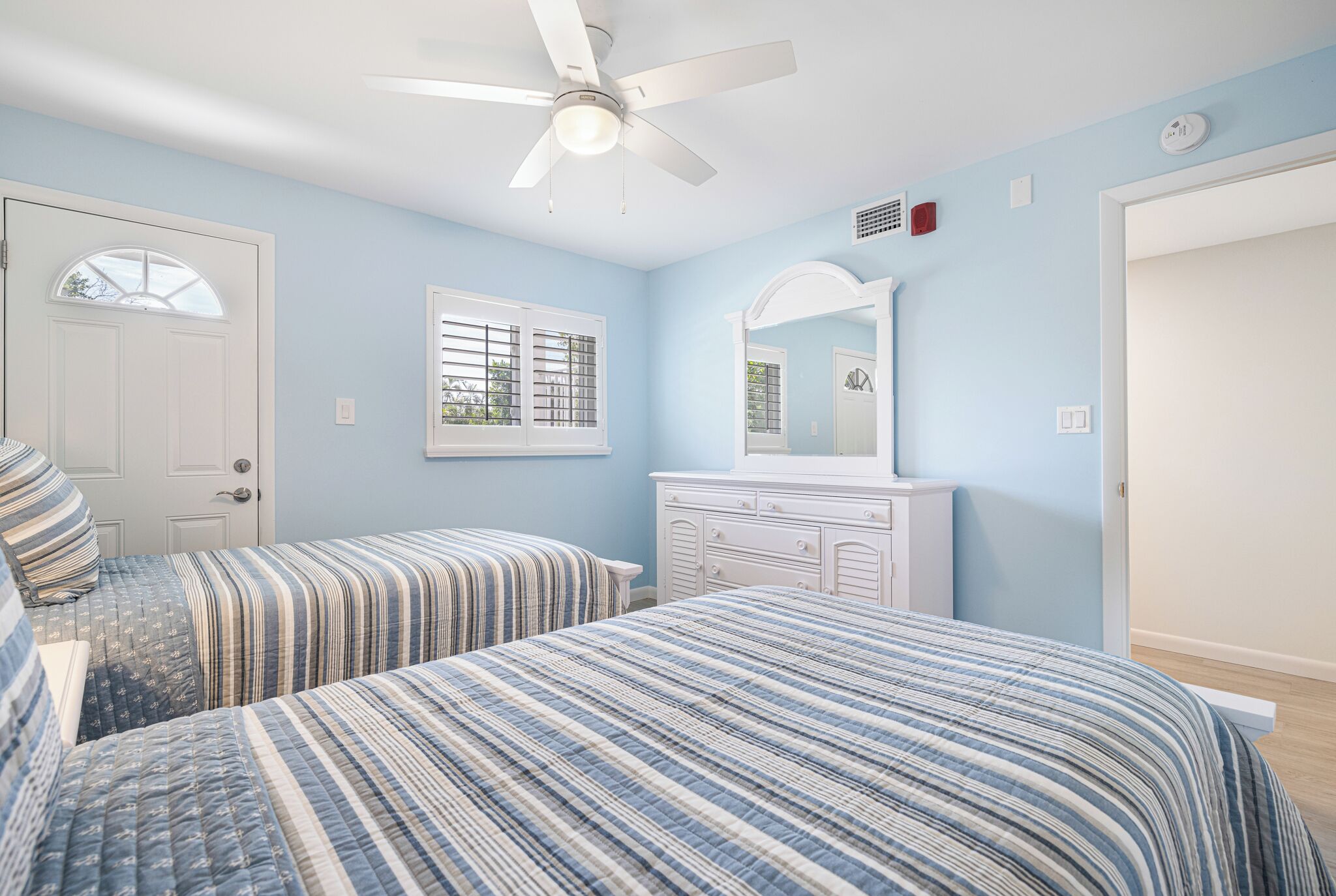 A bedroom with two beds, a ceiling fan, a dresser, and a window with shutters.