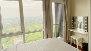 A hotel room with a large bed, a vanity with a mirror and lights, and a view of a cityscape through large windows. - Breeze Apartments at Bintaro by OkeStay (South Tangerang)