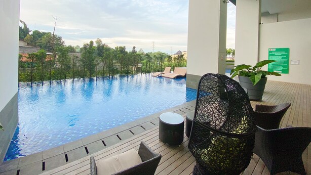A view of an infinity pool with lounge chairs, a wicker chair, and a potted plant. - Breeze Apartments at Bintaro by OkeStay (South Tangerang)