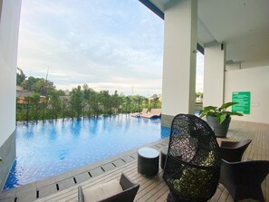 A view of an infinity pool with lounge chairs, a wicker chair, and a potted plant. - Breeze Apartments at Bintaro by OkeStay (South Tangerang)