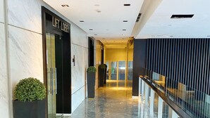A modern hotel lobby with a marble floor, a lift lobby sign, and a glass railing along the corridor. - Breeze Apartments at Bintaro by OkeStay (South Tangerang)