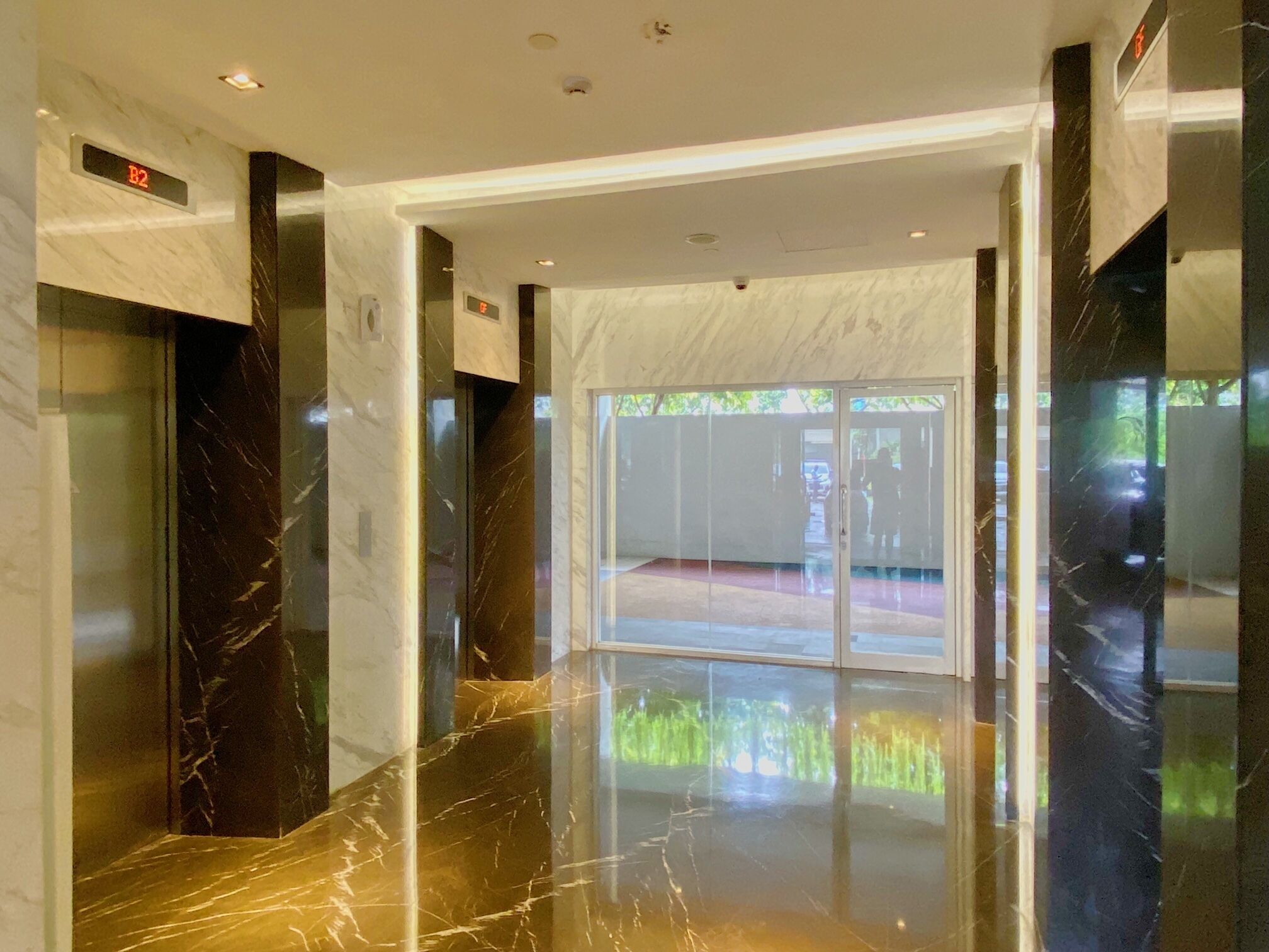Un hall d’entrée moderne avec un sol en marbre, des portes en verre et un écran numérique indiquant l’étage de l’ascenseur.