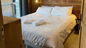 Una cama bien hecha con ropa de cama y toallas blancas, un cabecero de madera y una pared de acento de piedra.