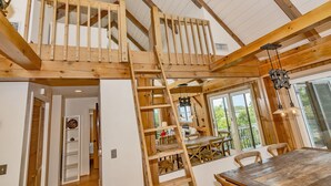 Un interior de madera con un entrepiso con dormitorio, una zona de comedor y vistas al exterior.